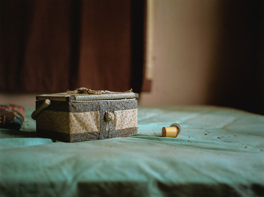A patterned fabric box with a braided handle and a yellow spool of thread rest on a dusty teal surface.